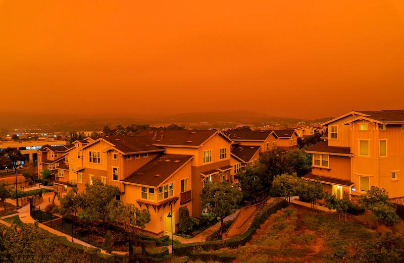 A suburban neighborhood under an orange sky caused by the glow of a nearby wildfire.