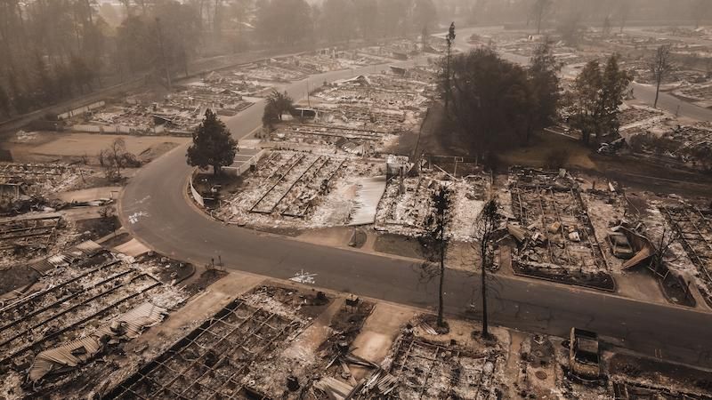 Aerial view of a community devastated by a wildfire, showing destroyed homes and charred landscapes.